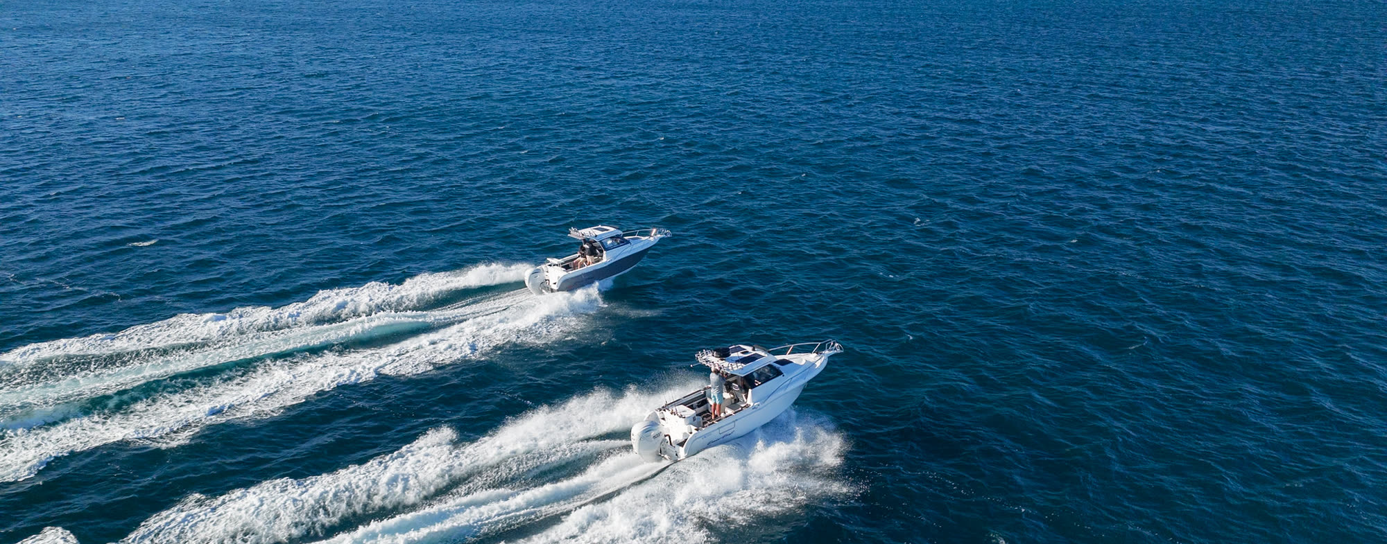 Two fishing boats heading out across deep blue water, seen from above