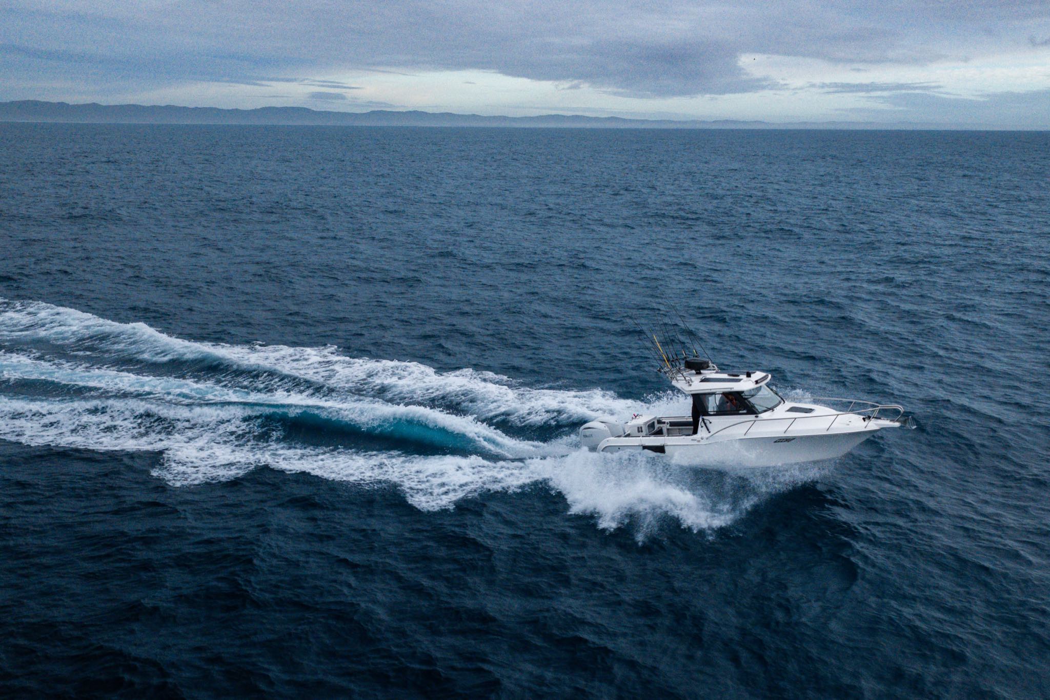 A fishing boat speeds across deep blue ocean, its white wake curving behind it